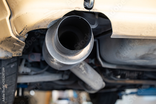 Low angle close up view inside a wide cannon exhaust tailpipe tip and rear muffler box on a vehicle elevated on a workshop lift.