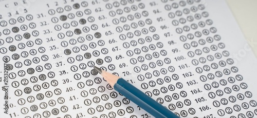 Blue pencil rests beside filled answer sheet. Circular choices mark student responses clearly. Paper shows rows of numbers and symbols. Test-taker focused, deliberate, concentrated