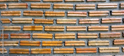 Textured brick wall with earthy tones. Rows of bricks lie neatly aligned. Gray mortar binds the pattern together. Wall shows signs of weathering and age. Ideal for rustic, vintage
