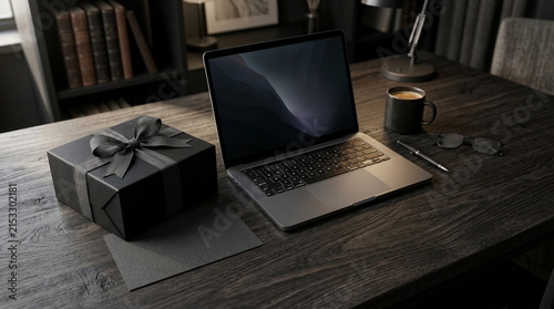 A sophisticated black gift box sits beside an open modern laptop on a dark wooden office desk.