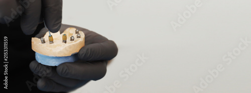 Doctor tightening a dental implant component with a surgical instrument on a jaw model, securing the implant during dental implant placement and prosthetic restoration procedure. banner copy space