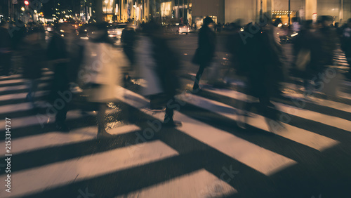 Blurry night scene of people crossing a busy street at a crosswalk.