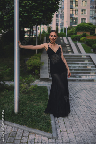 A beautiful woman in a luxurious black dress poses in the city