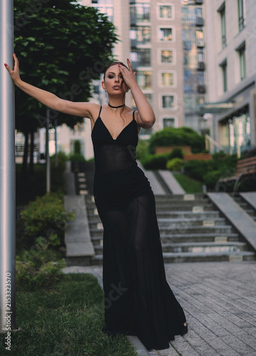 A beautiful woman in a luxurious black dress poses in the city