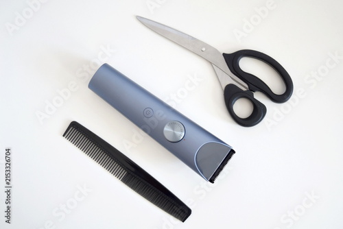 Flat lay composition of hair grooming essentials featuring a cordless electric trimmer, black hair comb, and stainless steel scissors neatly arranged on a clean white background.