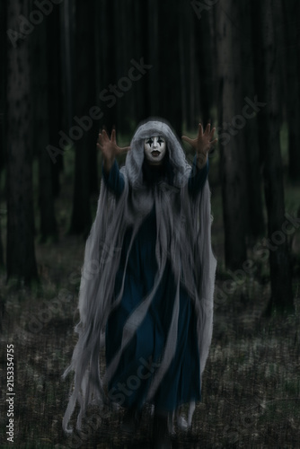 Spooky and scary Halloween themed image in a dark forest with smoke and an eerie woman with a mask. .
