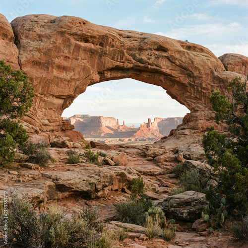 One large natural sandstone arch frames a distant landscape across an expansive desert landscape