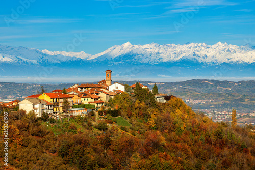 Small town among autumn trees and mountains on background in Piedmont, Italy.