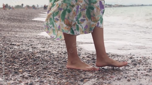 Woman's feet walking along a pebbly beach, while the waves crash against her toes