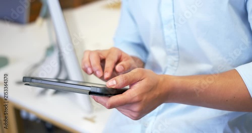 Man in blue shirt holding tablet case tapping top-left while swiping screen at desk, browsing app