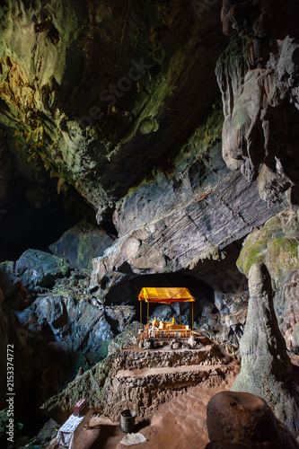 VANG VIENG, LAOS – A Buddha shrine glows with candlelight inside Tham Chang Cave near Vang Vieng, where sacred statues occupy the illuminated limestone cavern.