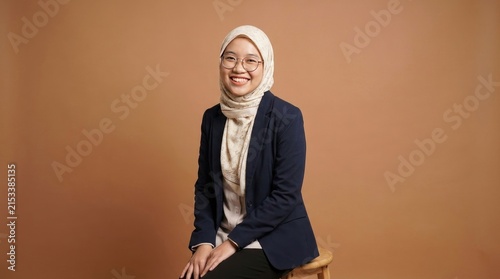 Smiling young business woman wearing a hijab and glasses against a neutral background