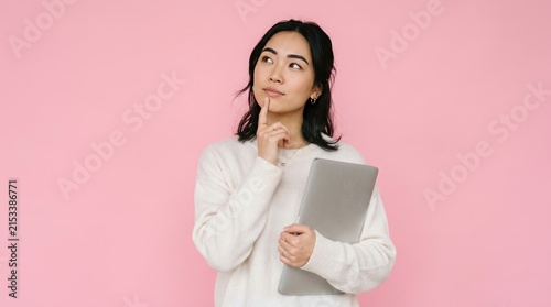 Thoughtful woman holding laptop against pink background