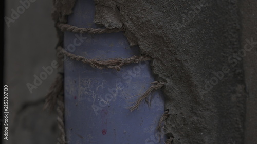 Weathered Blue Plastic Pipe Secured with Frayed Rope in Damaged Wall