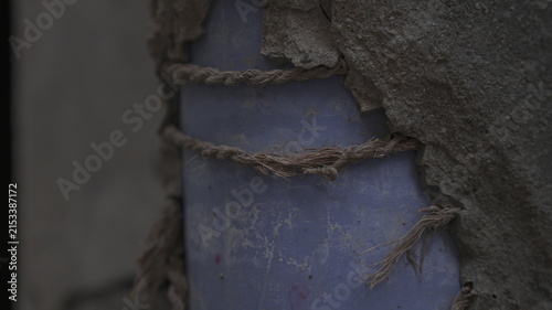Weathered Blue Plastic Pipe Secured with Frayed Rope in Damaged Wall