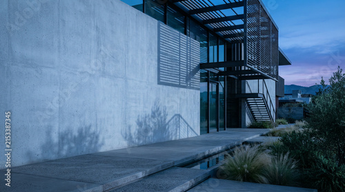 Modern two story concrete building with dark metal accents and landscaped grasses at dusk