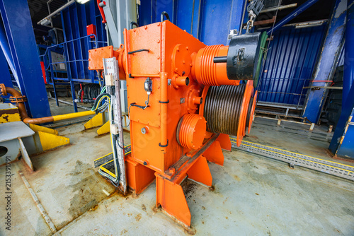 New York, United States - March 20, 2026: Heavy industrial cranes and cable spool on offshore vessel deck at port under cloudy sky