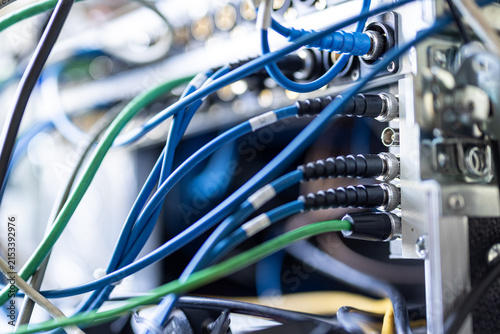 A detailed close-up of blue and green SDI and audio cables connected into the rear patch panel of a broadcast server rack in a professional production unit.