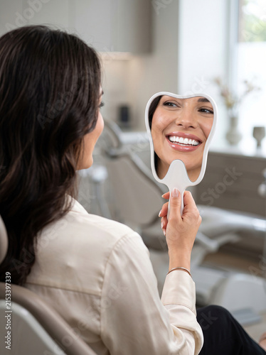 Mulher Sorrindo com Espelho com Formato de Dente em Consultório
