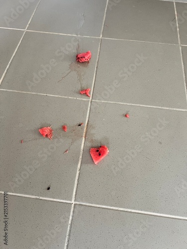 Фотография Smashed watermelon pieces scattered across gray tiled floor with red pulp and se