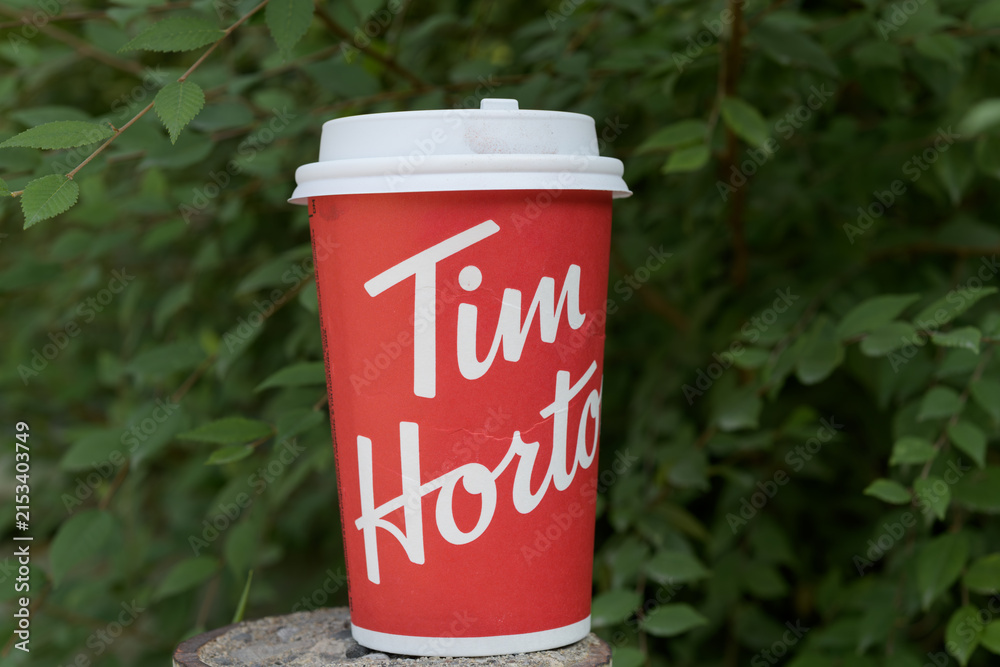 Fototapeta premium close-up of a discarded Tim Hortons beverage cup on a defocused foliage background in Toronto