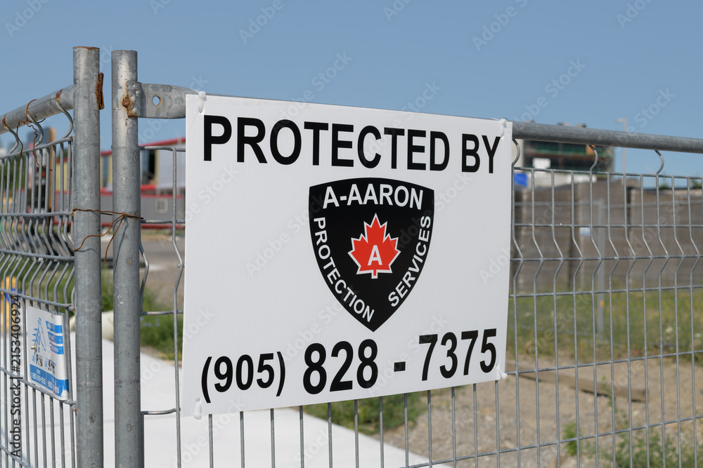 Fototapeta premium metal sign of A-AARON Protection Services fixed to a construction barrier fence, East York, Toronto