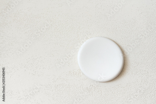 Round flat white stone pedestal placed against a close-up travertine surface in warm beige tones, with open copy space on the left and above for cosmetic advertising and beauty product presentation.