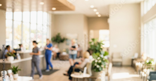 A modern and bright waiting area in a healthcare facility. People are seated and interacting in a space filled with plants and natural light.