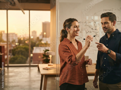 Woman and man discussing handwritten workflows on a whiteboard beside a sunset office window