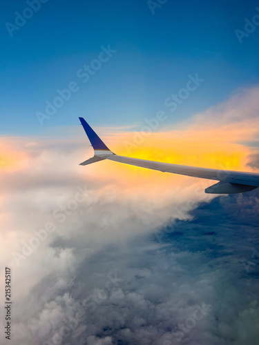 Vertical shot of airplane wing in the sky over clouds at sunset or sunrise