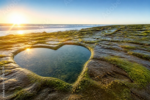 Heart shaped tide pool glowing on a rocky coast at sunrise