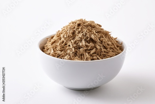 Shredded slippery elm bark in a small ceramic bowl on a white studio backdrop, side view