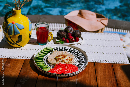 Oatmeal with cucumber, tomato and grilled halloumi cheese served on modern ceramic plate on terrace by pool
