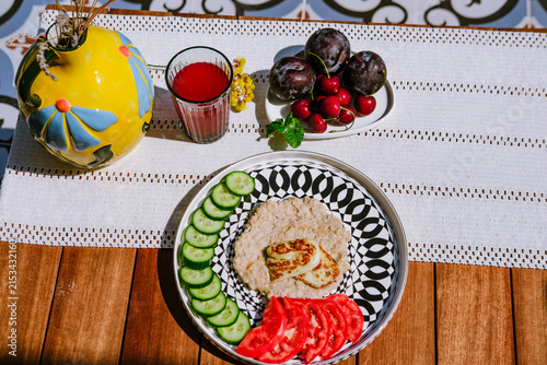 Oatmeal with cucumber, tomato and grilled halloumi cheese served on modern ceramic plate on terrace by pool