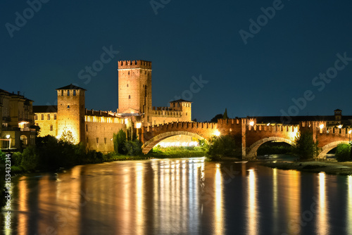 Illuminated Castelvecchio and Ponte Scaligero reflected in Adige river at night in Verona
