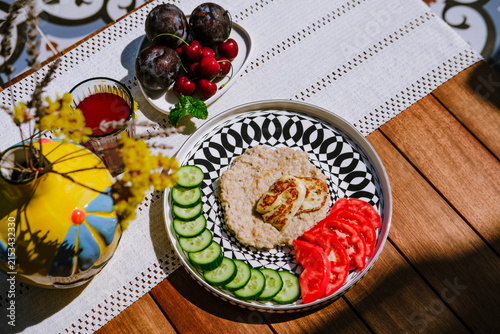 Oatmeal with cucumber, tomato and grilled halloumi cheese served on modern ceramic plate on terrace by pool