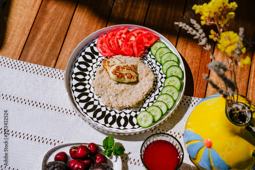 Oatmeal with cucumber, tomato and grilled halloumi cheese served on modern ceramic plate on terrace by pool