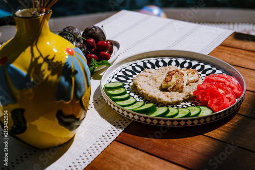 Oatmeal with cucumber, tomato and grilled halloumi cheese served on modern ceramic plate on terrace by pool