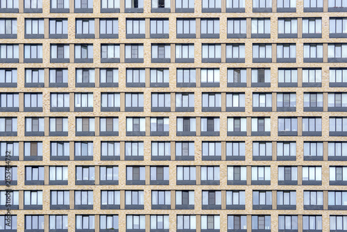 Yellow brick skyscraper facade with symmetrical glass windows grid. Repetitive modular pattern of modern residential apartment building exterior.