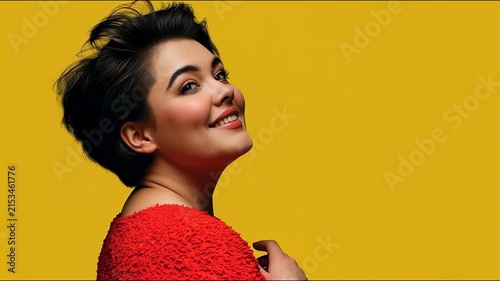 A smiling woman with short dark hair in a red textured top looks up joyfully against a vibrant yellow background.