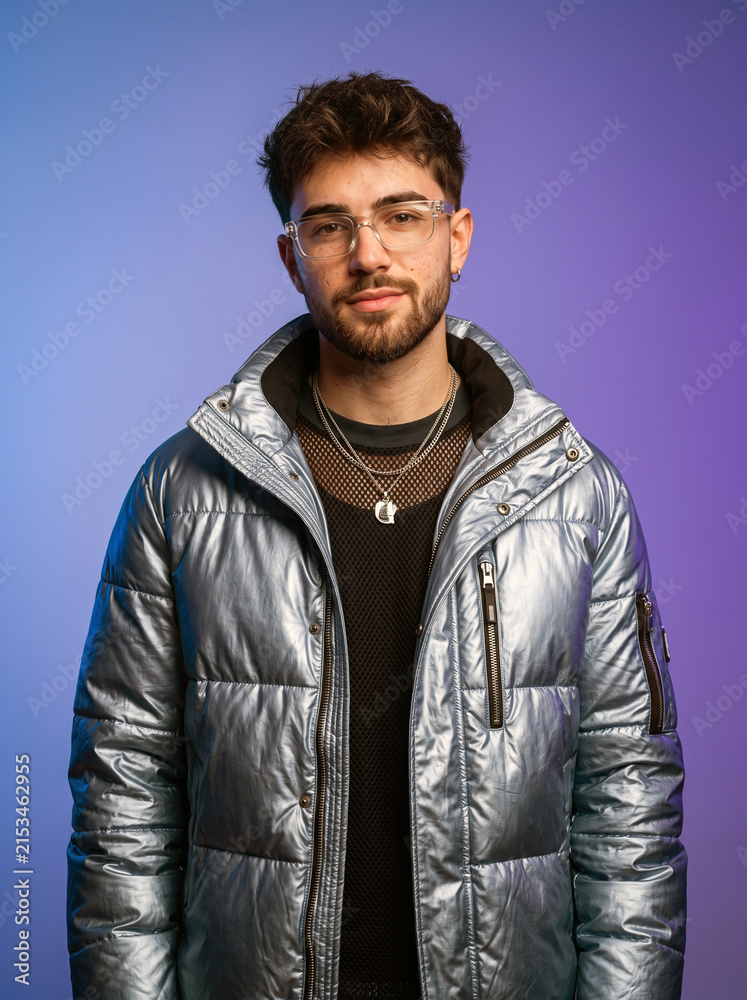 Fototapeta premium Young Man Wearing Glasses and Puffer Jacket Posing Against Gradient Background