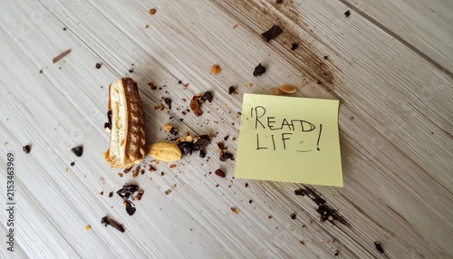 Sticky note with handwritten message on messy wooden floor.