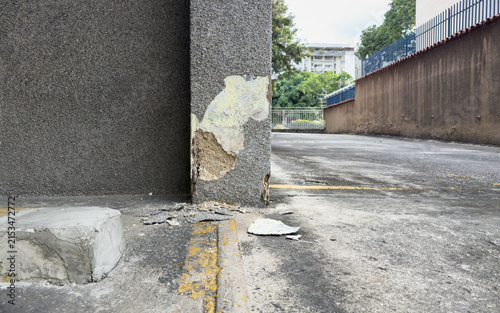 Damaged concrete pillar with flaking plaster and fallen debris in the parking lot – Building maintenance issue