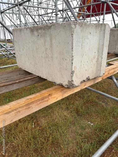 Photography Concrete barrier block resting on wooden planks beside metal scaffolding at an outdoor construction site