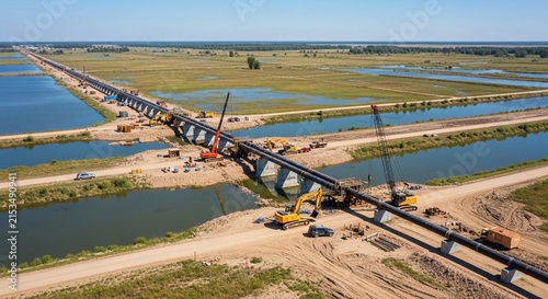 Extensive pipeline construction project underway across water and rural landscape with heavy machinery and cranes