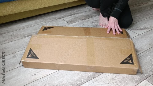 Person cutting open cardboard box with utility knife on wooden floor
