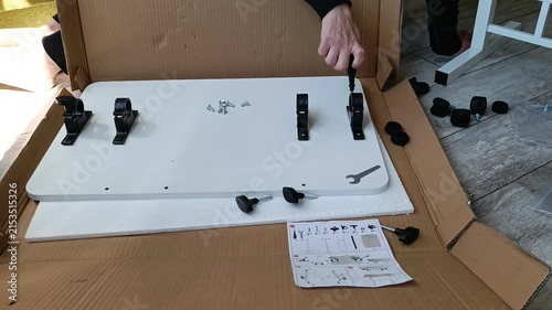 Person assembling flat pack furniture with tools and hardware on wooden floor