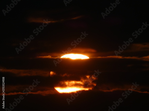Fotografía Sunset sun disk split by horizontal dark cloud bands