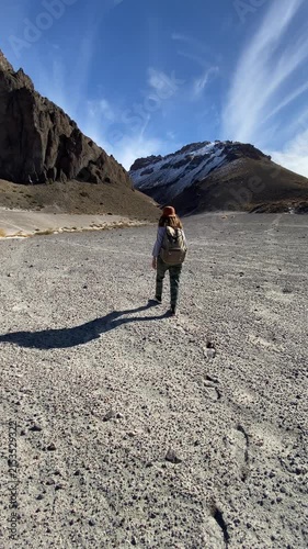 Young Latina woman walking through an arid landscape with mountains in the background, captured in a casual cellphone-recorded outdoor clip.