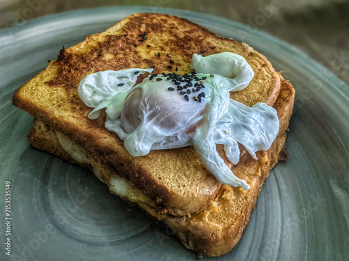 Obraz na płótnie Close up view of crispy toasted sandwich topped with a poached egg and black ses